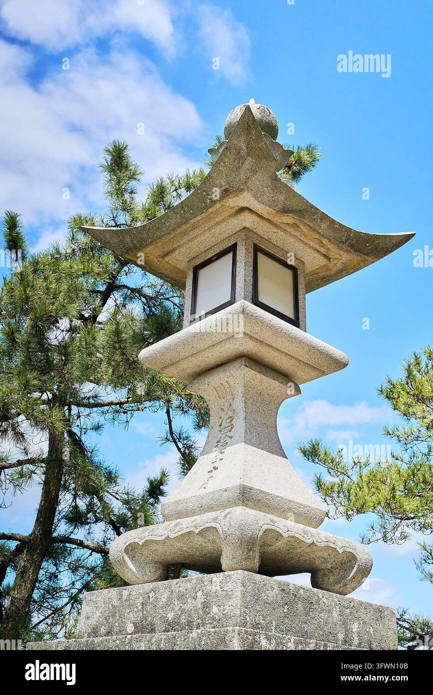 Lanterne japonaise en pierre traditionnelle avec un toit élégant de style pagode contre un ciel bleu, entourée de pins au Japon. Banque D'Images