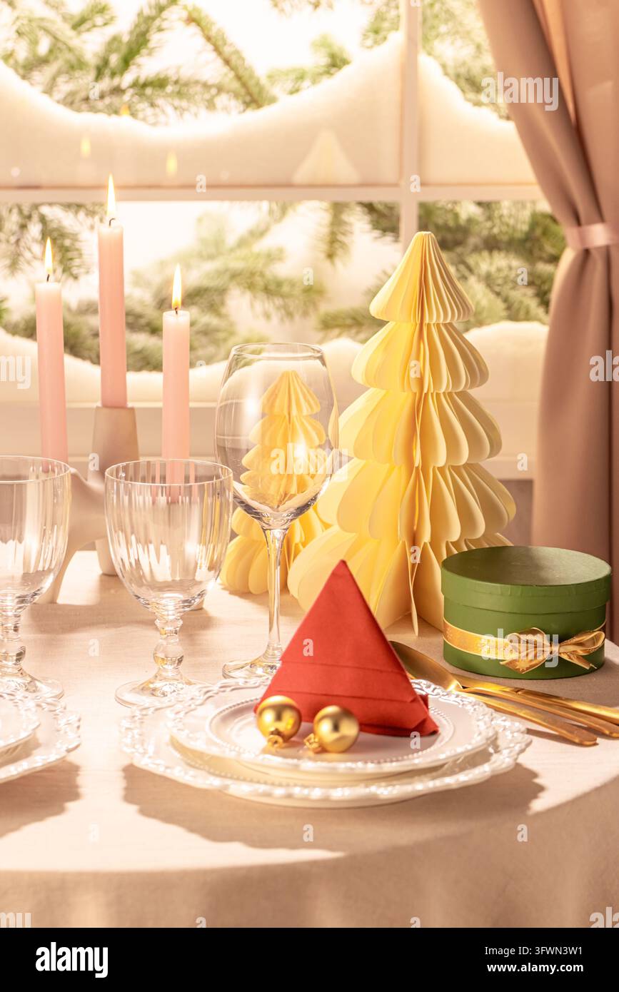 Vue verticale détaillée d’un couvert de table festif comprenant un arbre en serviette rouge pliée, des boules dorées, de la verrerie en cristal, un arbre en papier crème, un coffret cadeau vert Banque D'Images