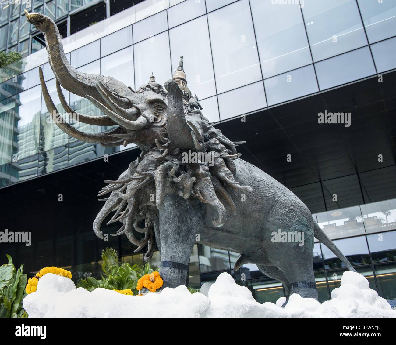 Statue en bronze détaillée d'un éléphant mythologique à plusieurs têtes debout devant la façade en verre moderne d'un gratte-ciel contemporain à Bangkok. Banque D'Images