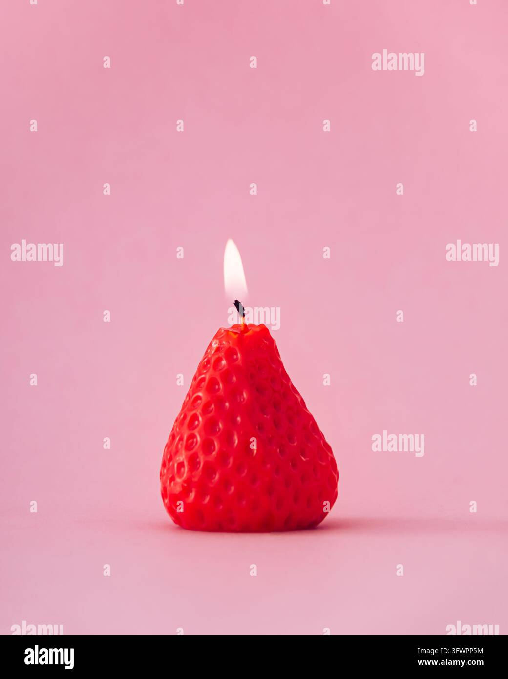 Bougie en forme de fraise en train de brûler sur fond rose. Esthétique estivale créative et concept de nature morte minimaliste. Banque D'Images