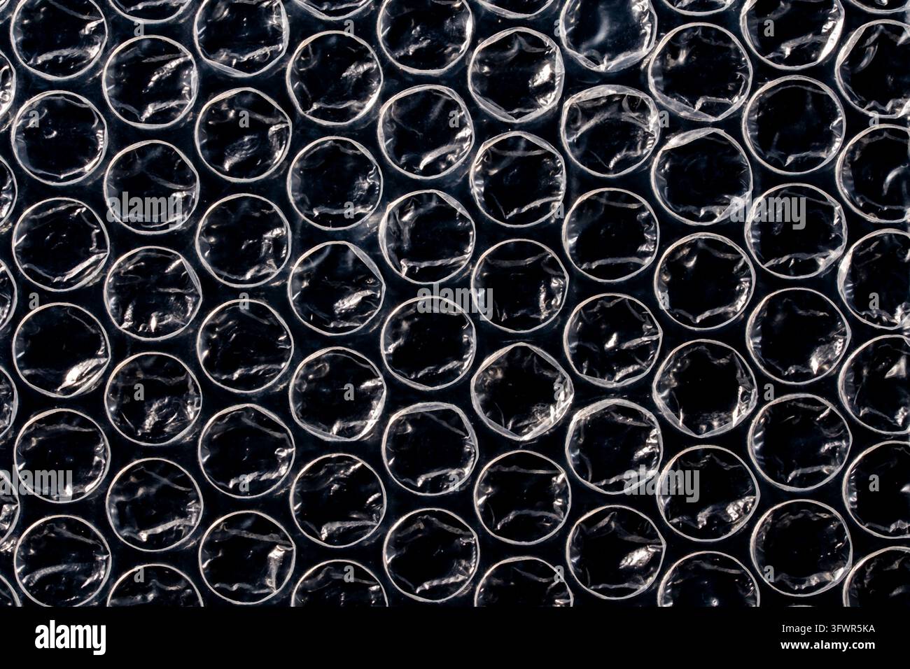Texture de film à bulles transparent en plein cadre sur fond noir. Vue de dessus d’une feuille de film à bulles d’air en plastique clair. Fond macro de protection Banque D'Images