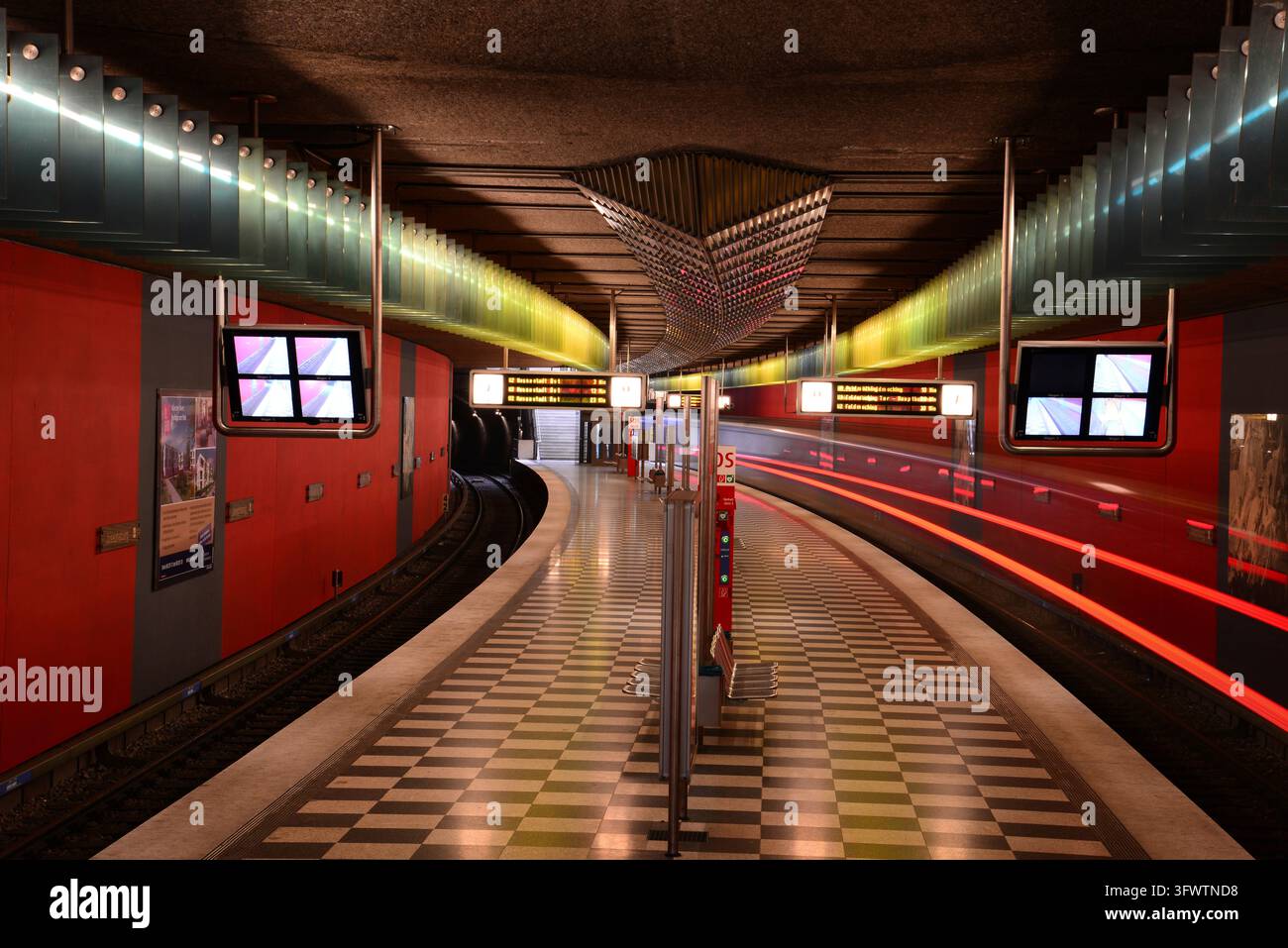 Une plateforme de métro incurvée avec un sol à damier et un train qui passe, station de métro Josephsburg, Munich, Bavière, Allemagne Banque D'Images