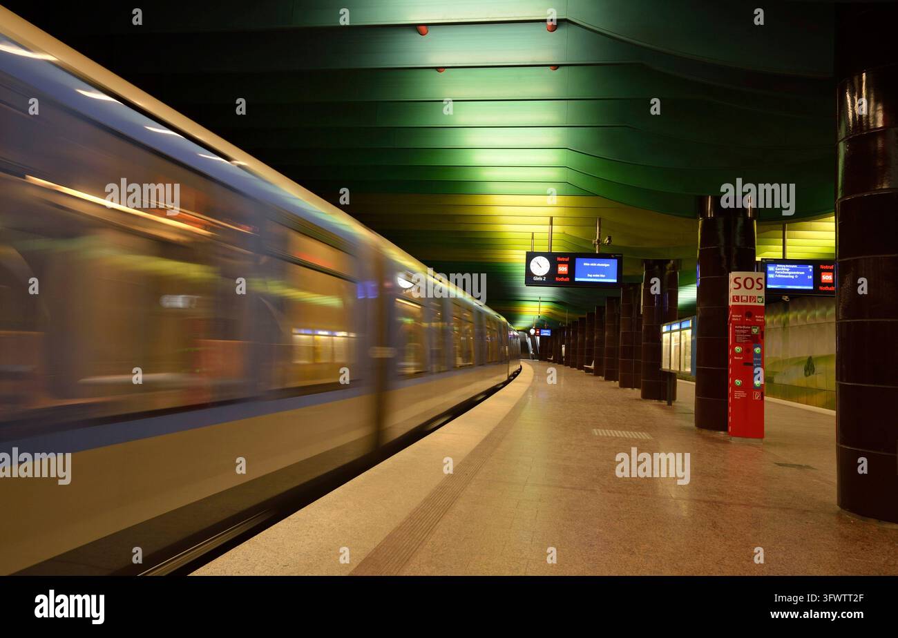 Un train flou qui passe devant une plateforme souterraine déserte avec un plafond vert et une colonne SOS rouge, métro, Clinique Großhadern, Munich, Bavière, All Banque D'Images