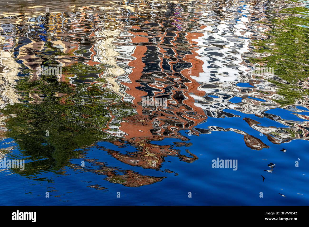 Réflexion colorée des bâtiments et des arbres dans l'eau, les formes semblent douces et déformées, la lumière crée des motifs vibrants de bleus, de verts et de rouges, w Banque D'Images