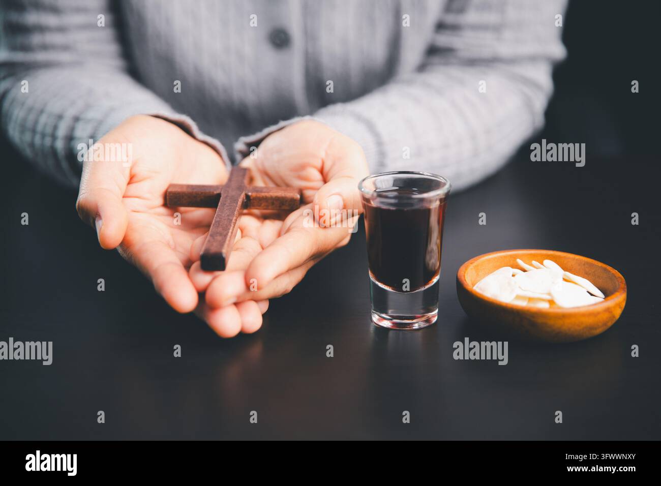 Mains tenant une croix en bois à côté d'hosties et d'une boisson rouge foncé, créant une scène solennelle d'adoration chrétienne pour la foi, la prière, le reste sacré Banque D'Images