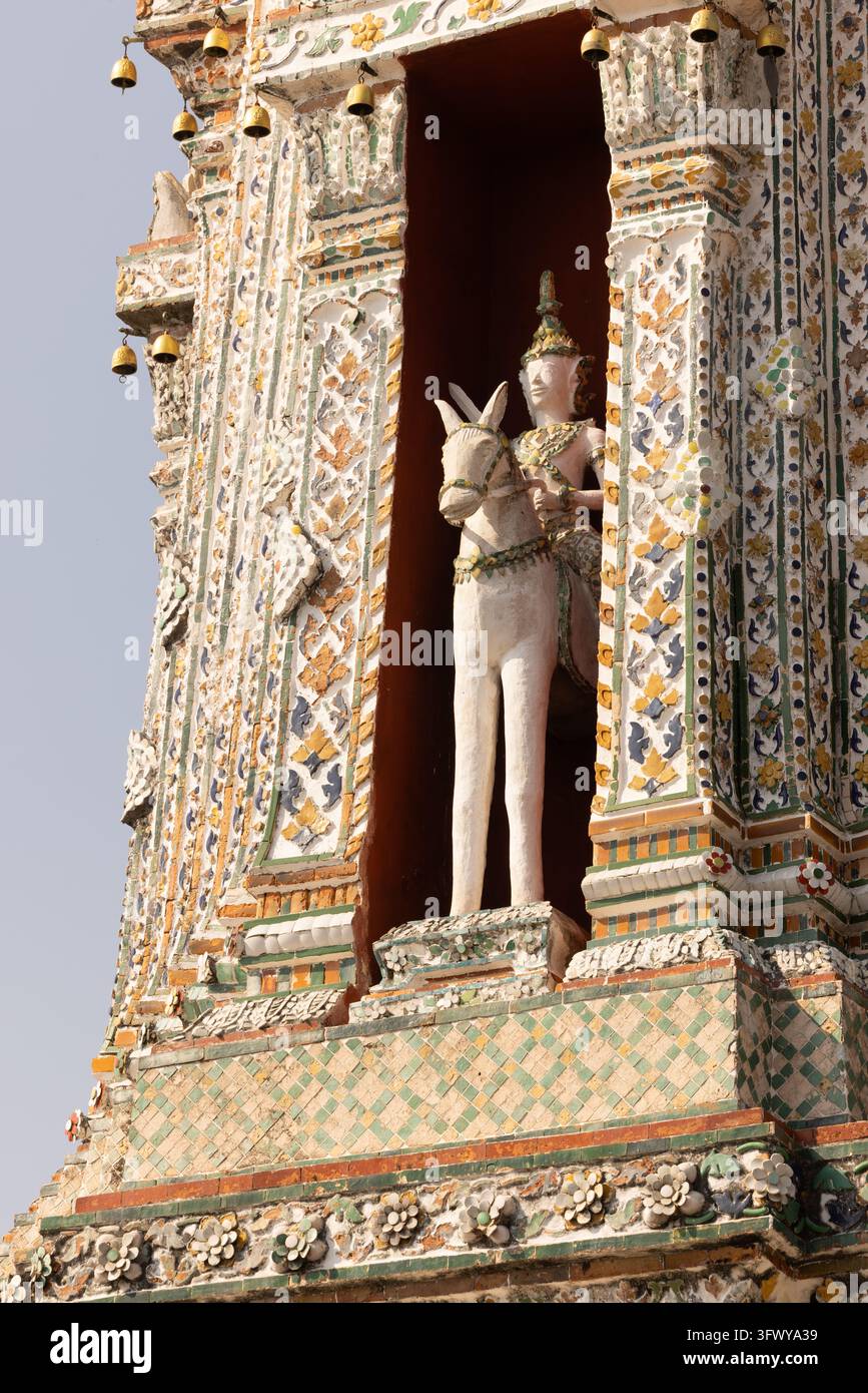 Bangkok, Thaïlande - 1er février 2026 : Une statue blanche d'une figure gardienne tenant des rênes se dresse dans une niche finement décorée d'un temple… Banque D'Images