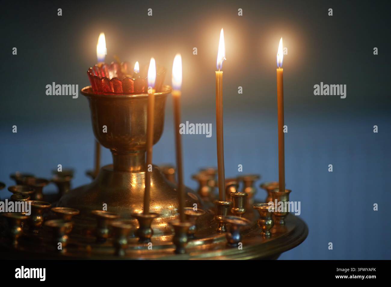 Porte-bougie d'église avec des bougies allumées dans un cadre religieux traditionnel. Chandelier en laiton avec plusieurs flammes et un porte-votif en verre rouge Banque D'Images