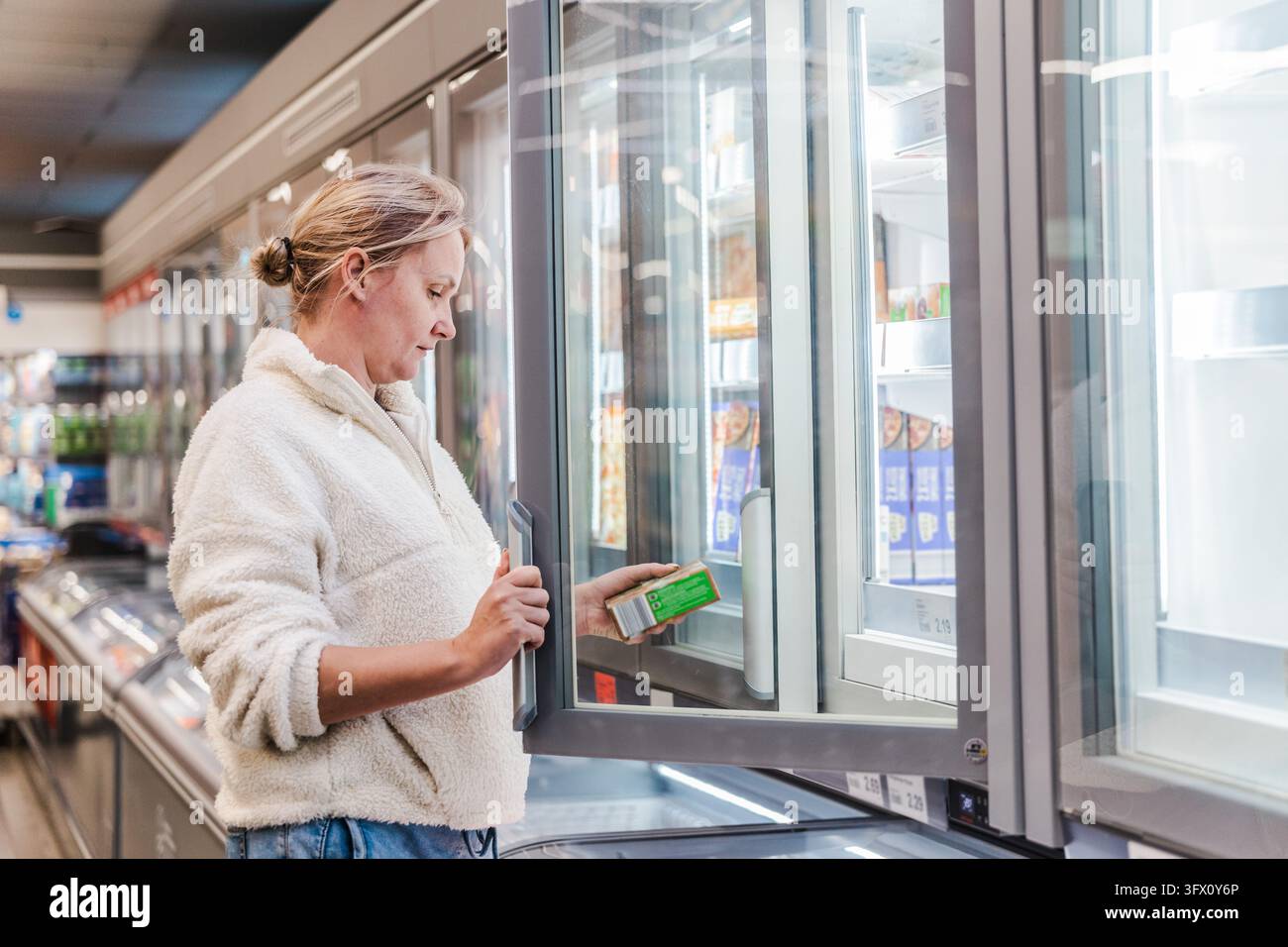 Une femme ouvre une vitrine réfrigérée tout en choisissant un produit dans un supermarché. Banque D'Images