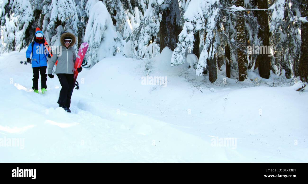 Des jeunes adultes avec des planches à neige traversent une forêt enneigée, profitant d'une sortie sportive hivernale. Banque D'Images