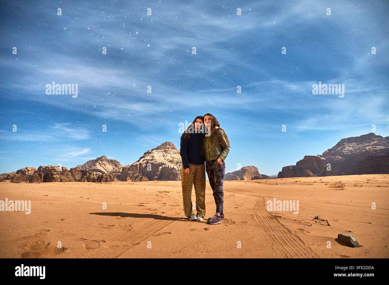 Deux voyageuses s'embrassant sous un ciel nocturne étoilé et strié de nuages à Wadi Rum, en Jordanie. Amitié, solidarité, aventure partagée et vacances mémorables dans le désert entourées de montagnes de grès Banque D'Images