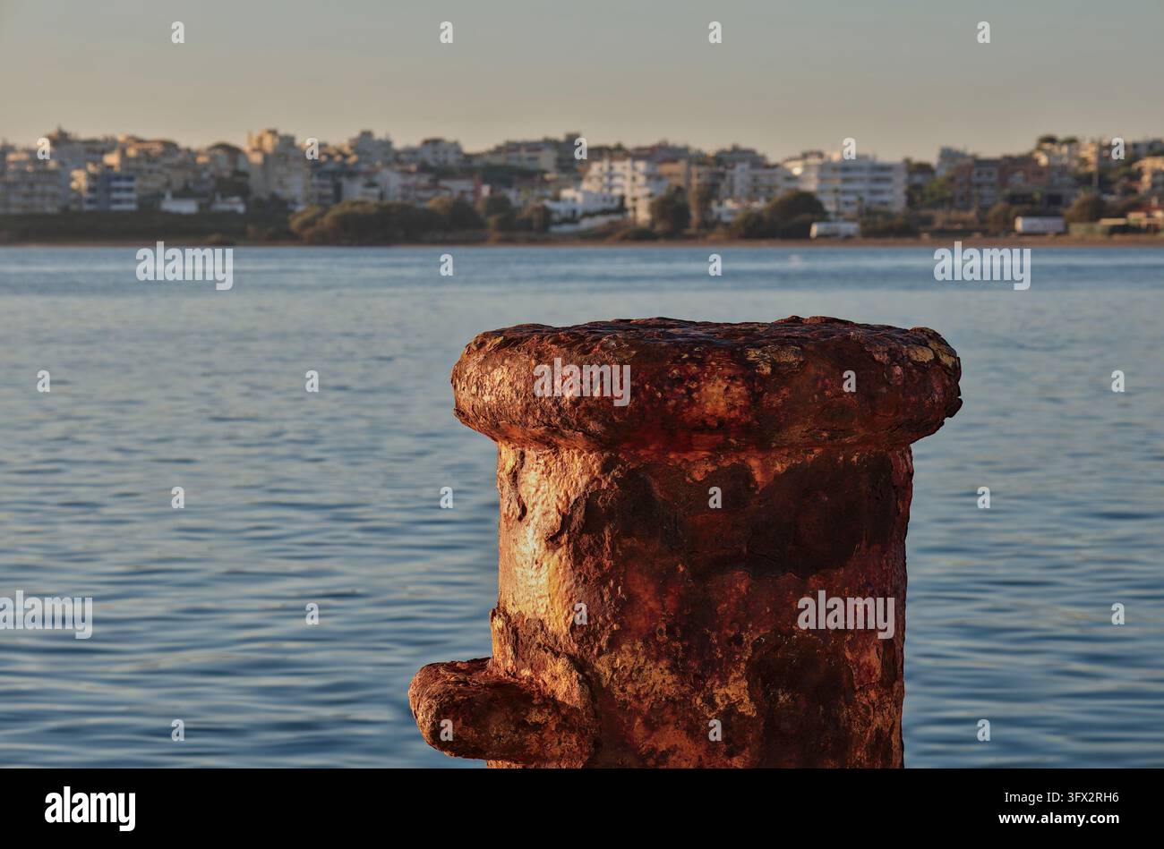 Poulie d'amarrage fortement corrodée sous un soleil chaud, avec la mer et un arrière-plan flou du front de mer, Rafina, Attique orientale, Grèce. Banque D'Images