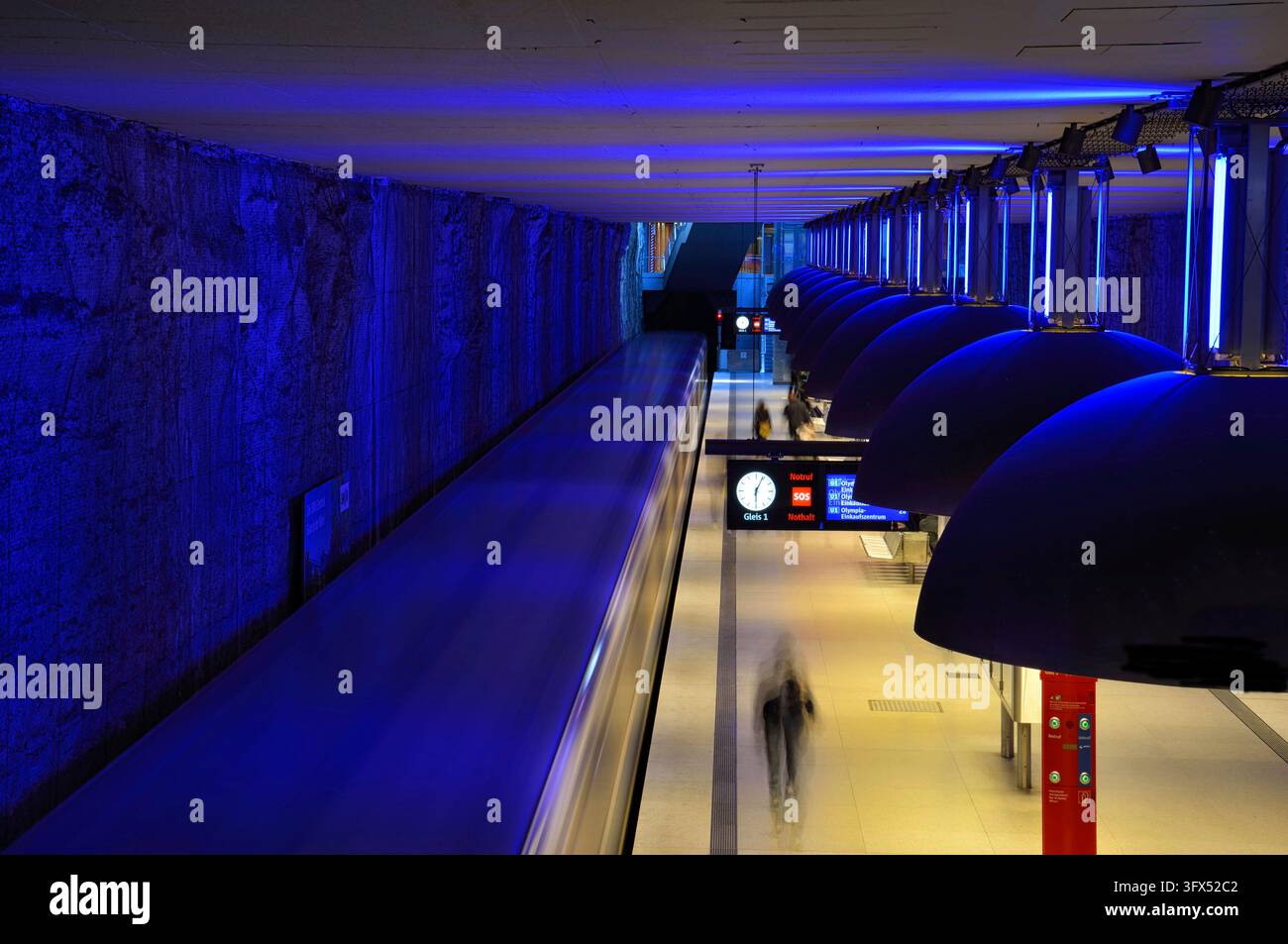 Des bandes de lumière bleue et des lumières noires guident le regard le long d'un quai de métro avec des passagers qui passent, station de métro Westfriedhof, Munich, Bavière, G Banque D'Images