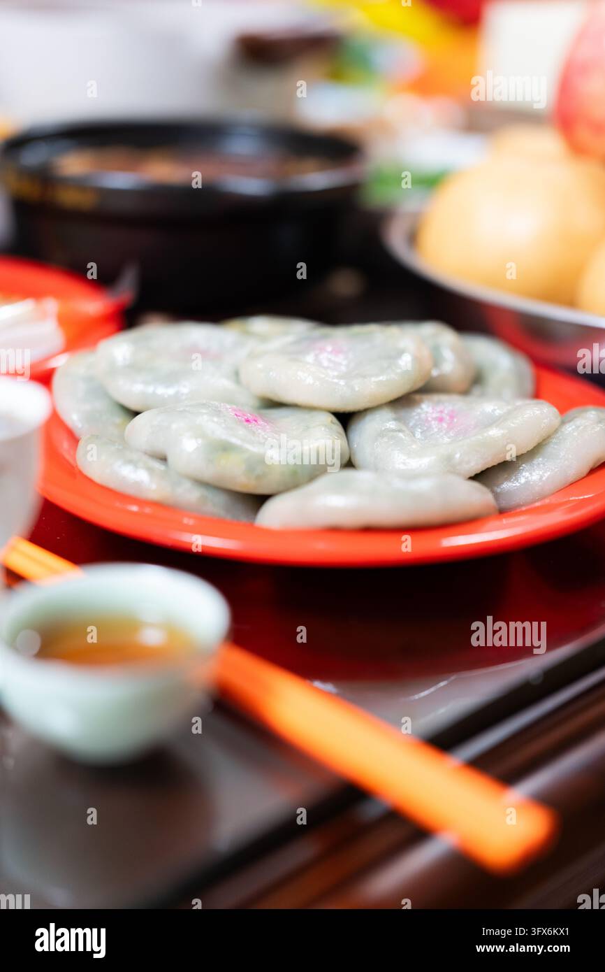 Gâteaux de riz coréens songpyeon cuits à la vapeur disposés sur une assiette rouge vif, garnis de garnitures sucrées et décorés de motifs floraux roses, servis pendant la fête des récoltes Chuseok avec du thé, des baguettes et des fruits de saison dans un cadre intérieur chaleureux Banque D'Images