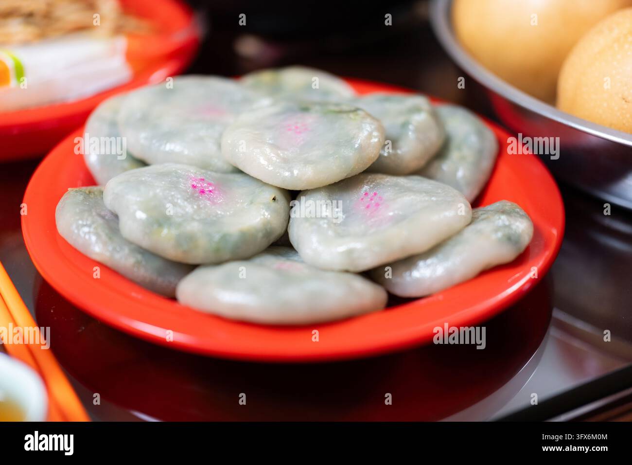 Gâteaux de riz coréens Songpyeon cuits à la vapeur avec mugwort vert et teinture florale rose, servis dans une assiette rouge vif pendant la fête de récolte Chuseok, symbolisant la gratitude et la prospérité dans la cuisine coréenne traditionnelle Banque D'Images