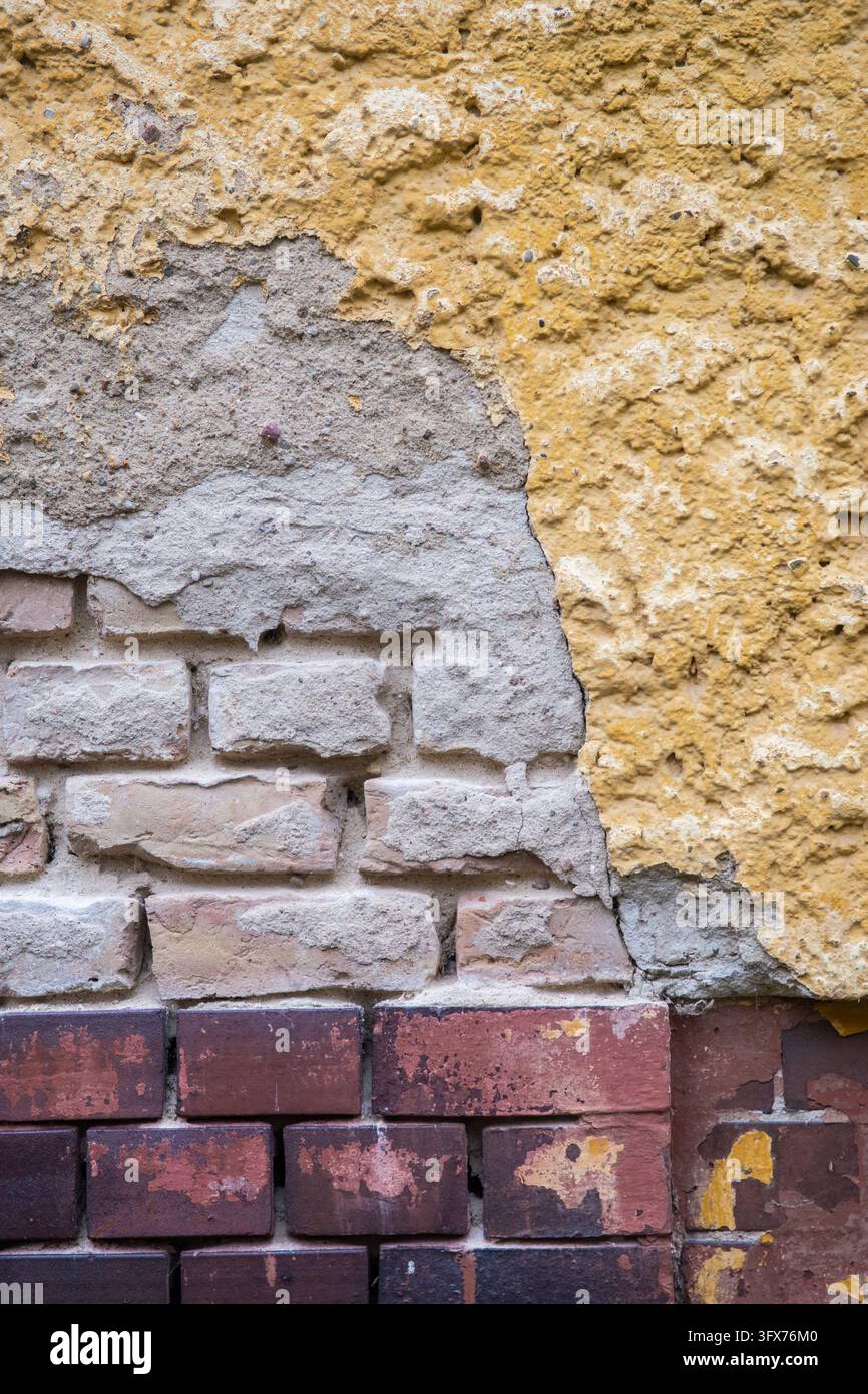 Détail rapproché de plâtre ocre écaillé et de briques pâles exposées au-dessus d'une base en briques rouge foncé sur un mur patiné à Berlin, Allemagne. Banque D'Images