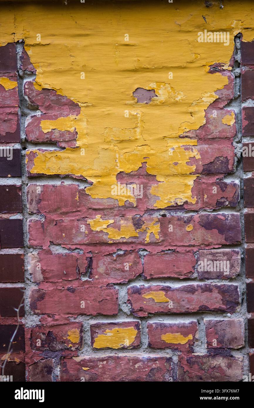 Grossissement de peinture jaune écaillée sur une brique rouge révélant des couches de maçonnerie et de plâtre érodées sur un bâtiment à Berlin, Allemagne. Banque D'Images
