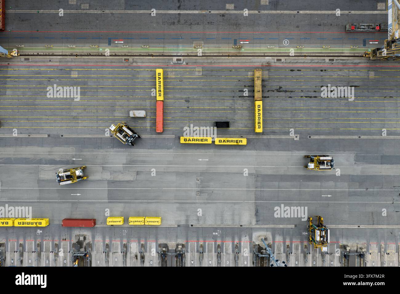 Les véhicules guidés automatiquement naviguent à travers un terminal d'expédition pavé en plein jour, manœuvrant avec précaution des barrières de chargement jaunes et des conteneurs sur Banque D'Images