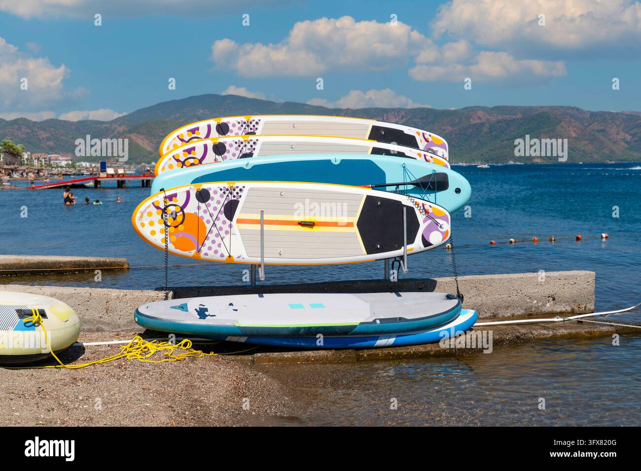 Planches de stand-up paddle (SUP) colorées disposées sur un rack de location dans une station balnéaire, prêtes à être louées. Photo conceptuelle représentant du matériel de sports nautiques Banque D'Images