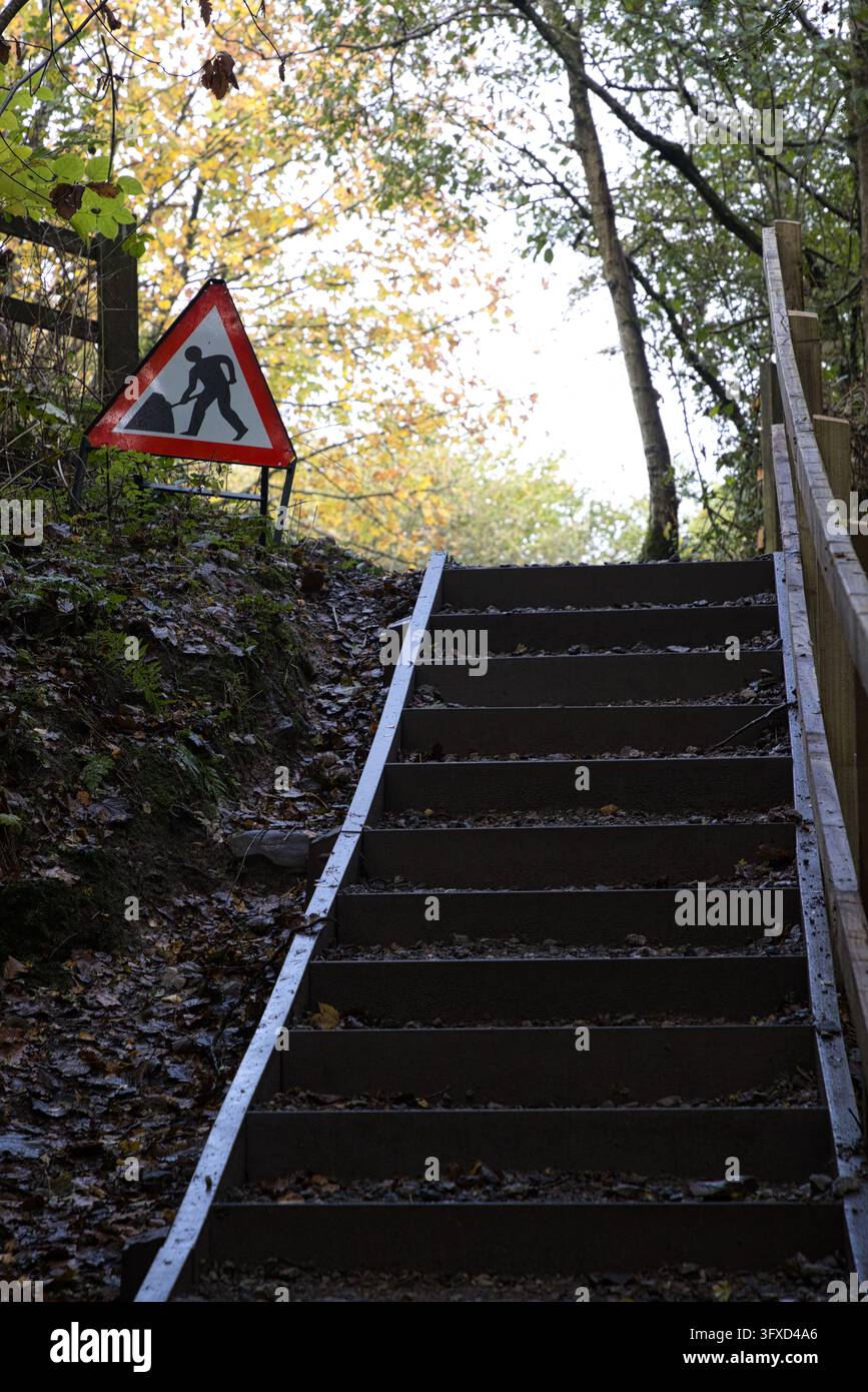 Escalier extérieur en métal avec un panneau d'avertissement de travaux routiers dans un cadre boisé au Moses Gate Country Park, Bolton, Lancashire, Royaume-Uni. Banque D'Images