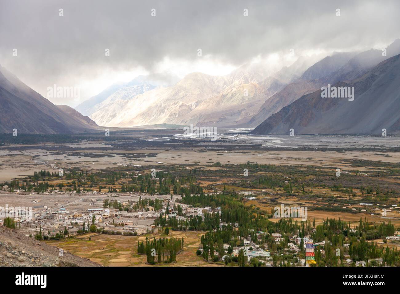 Village avec des peupliers dans une large vallée fluviale sous des nuages orageux et des montagnes, Ladakh, Turtuk, Inde Banque D'Images