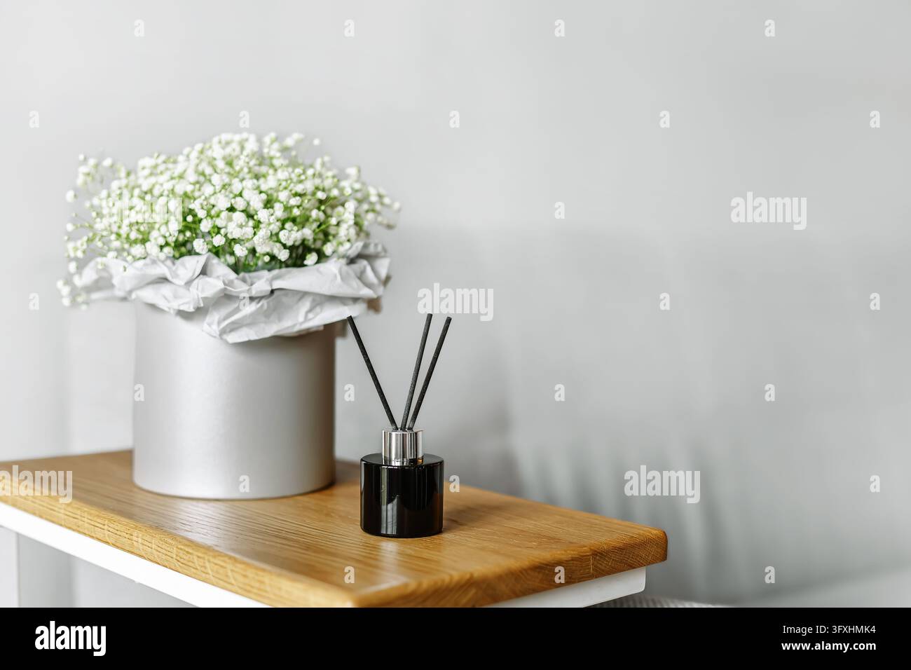 Flasche diffuseur d'arômes en verre noir et délicates fleurs de gypsophile blanches dans une boîte à chapeau en argent posée sur une table en bois dans une pièce confortable. Minima Banque D'Images