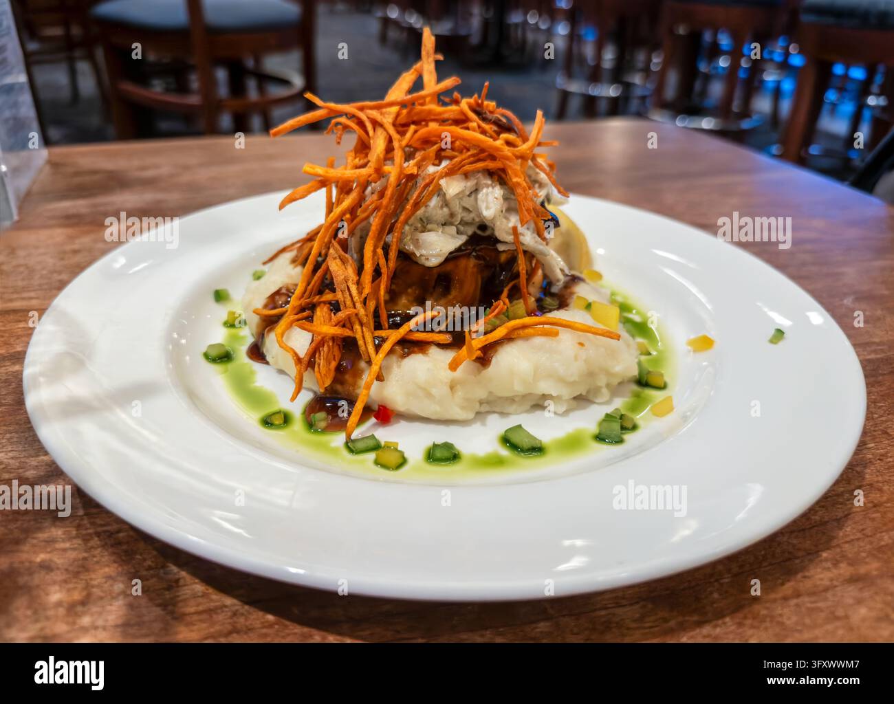 Côte de bœuf braisée servie sur une purée de pommes de terre crémeuse, garnie de chair de crabe, de patate douce croustillante, d'une riche réduction brune et d'une huile aux herbes vibrante Banque D'Images