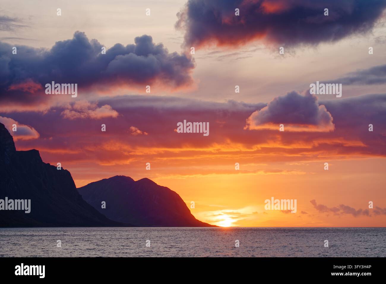 Couchant sur la côte près de Storvik le long de la Kystriksveien (Fv17) dans le Nordland, en Norvège. Le soleil bas est juste au-dessus de l'horizon, illuminant les formations nuageuses Banque D'Images