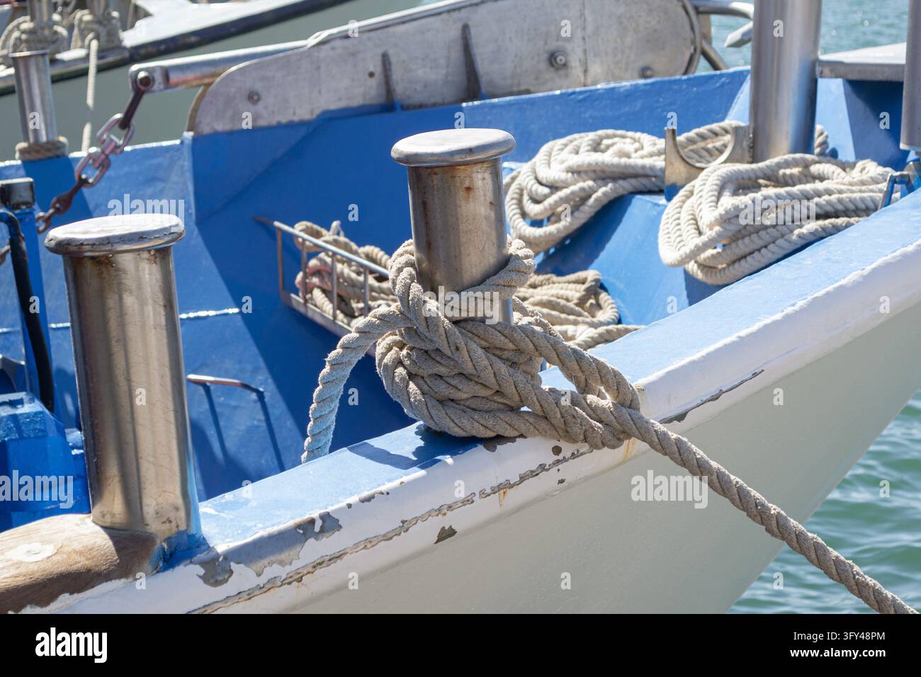 Corde d'amarrage enroulée autour d'un bollard en métal sur un bateau bleu et blanc Banque D'Images