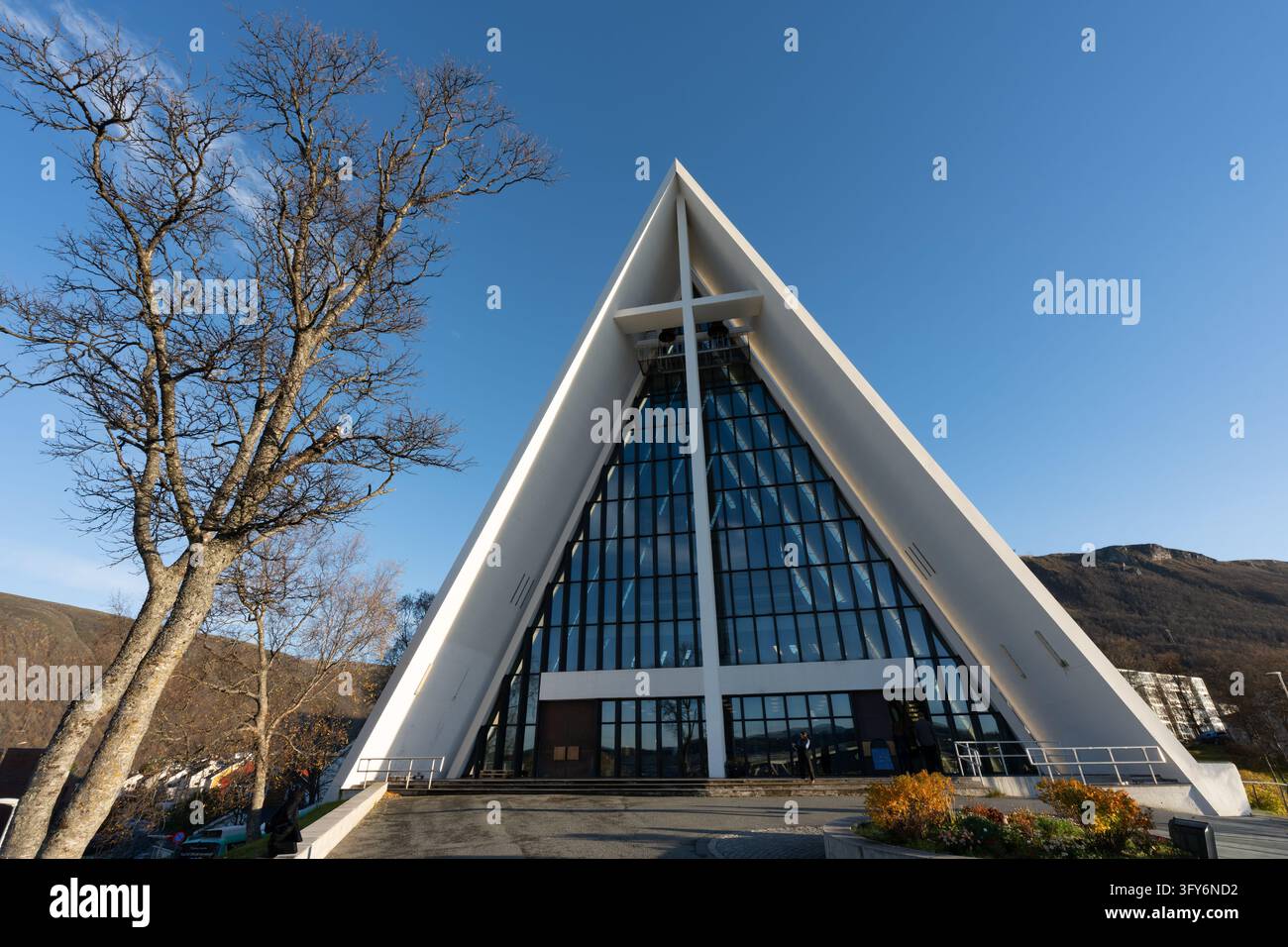 Cathédrale arctique (Ishavskatedralen ou église de Tromsdalen) à Tromsø, Norvège, avec sa façade triangulaire distinctive, des arbres et un fond montagneux. Banque D'Images