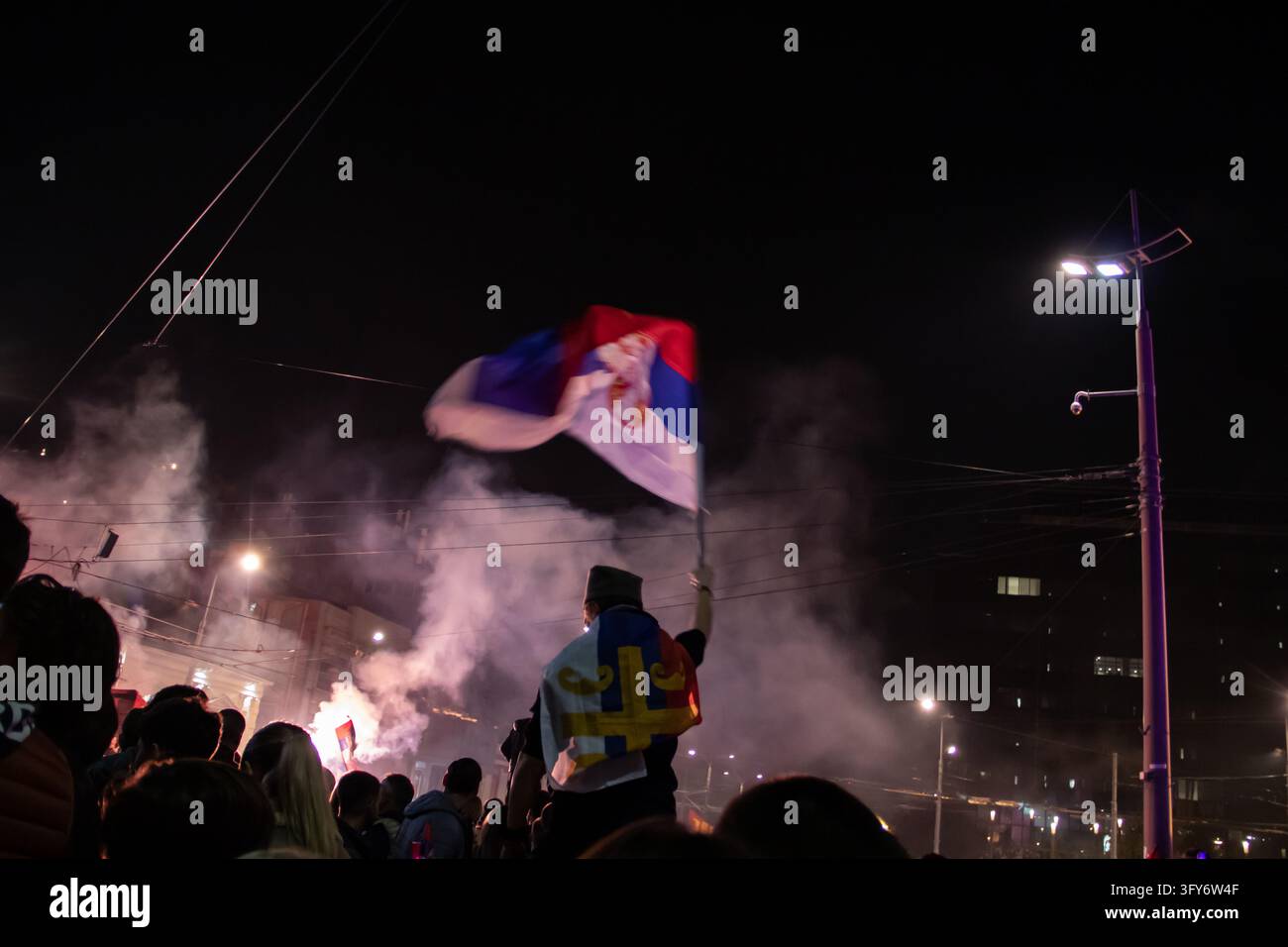 Une personne agite un drapeau en l'air la nuit, avec une foule de personnes rassemblée autour. Le drapeau est rouge, blanc et bleu, et la personne porte un d Banque D'Images
