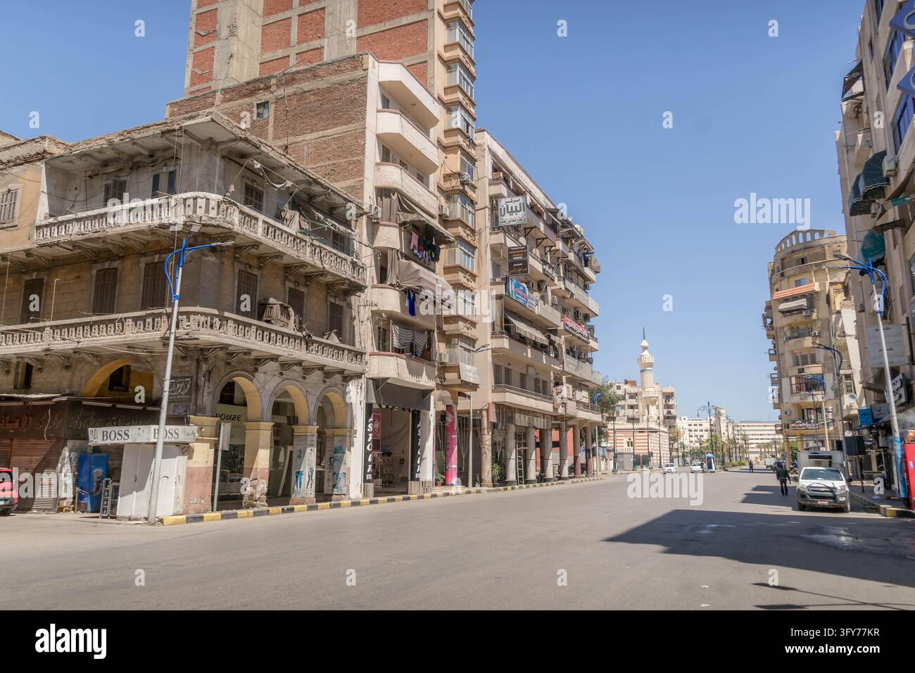 Architecture d'époque coloniale avec des arcades cintrées et un minaret le long d'une avenue urbaine déserte dans la ville portuaire historique de Port-Saïd, Égypte. Banque D'Images