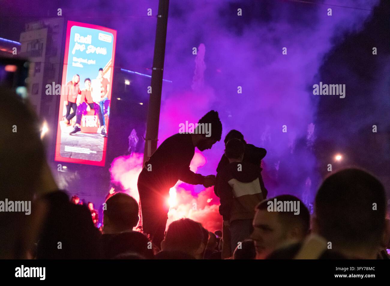 Une foule se rassemble sur la place Slavija à Belgrade, en Serbie, lors d'une célébration de la nuit des élections. La scène comprend un grand écran affichant une politique Banque D'Images