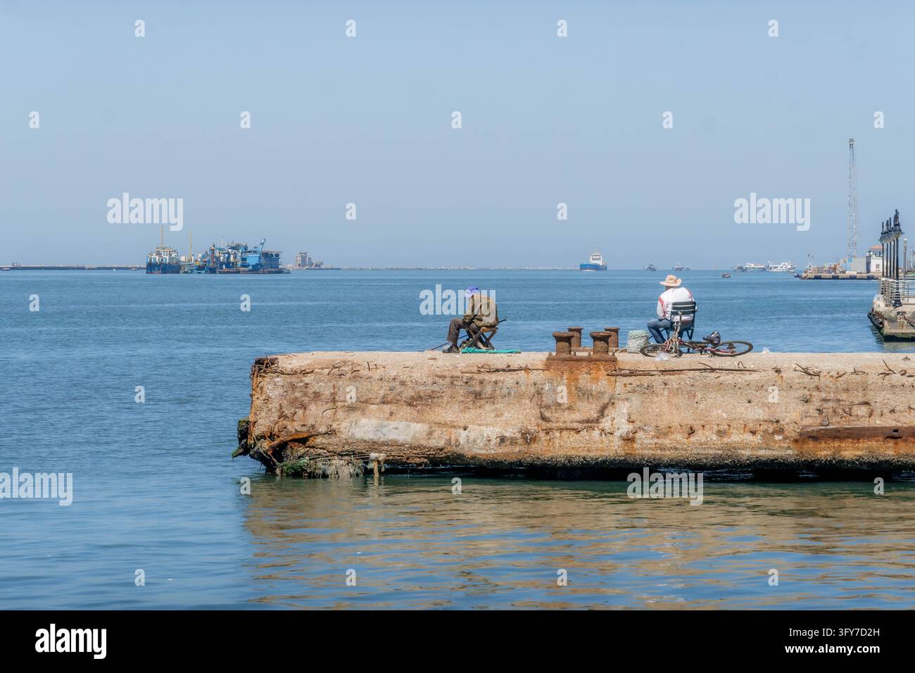 Des hommes locaux pêchent depuis un pier en béton érodé pour leur subsistance quotidienne le long du canal de Suez à Port-Saïd, en Égypte. Banque D'Images