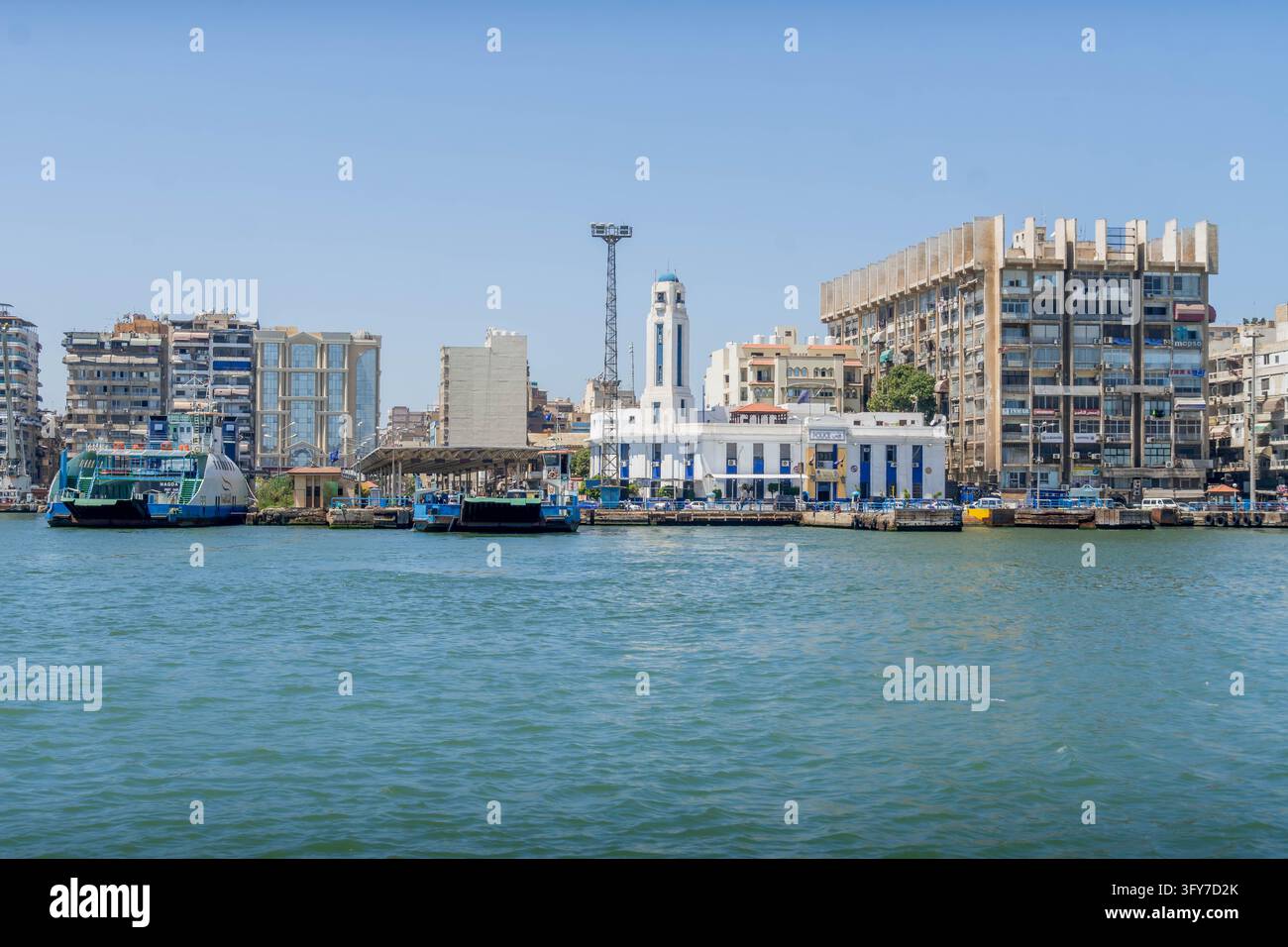 Paysage urbain du front de mer et terminal de ferries avec des navires à quai le long de la voie maritime animée du canal de Suez à Port-Saïd, Égypte. Banque D'Images