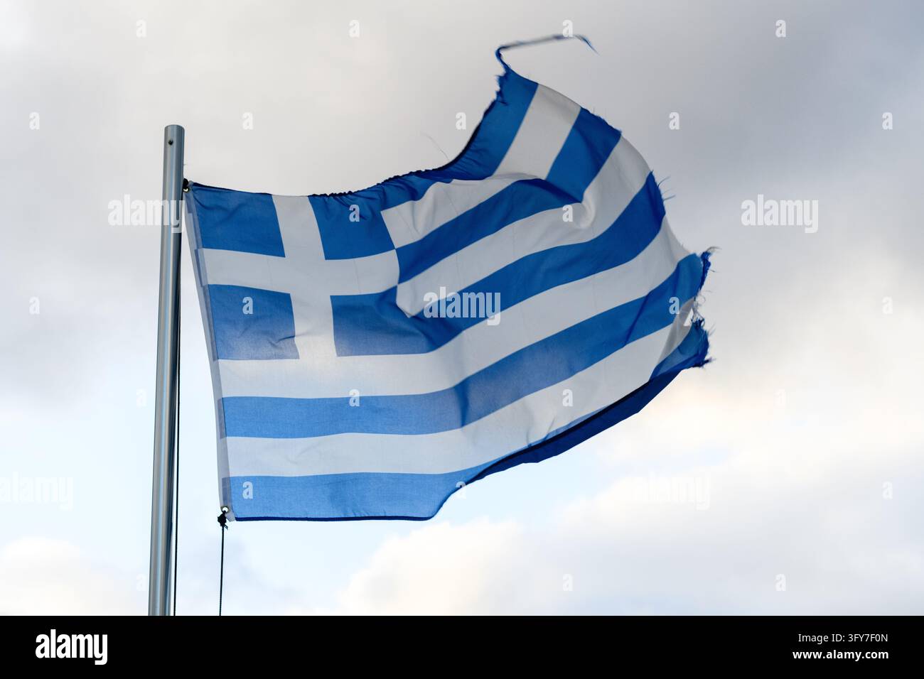 Un drapeau national grec usé, bleu et blanc aux bords effilochés, flotte fièrement dans le vent contre un ciel bleu clair, symbolisant la fierté nationale et Banque D'Images