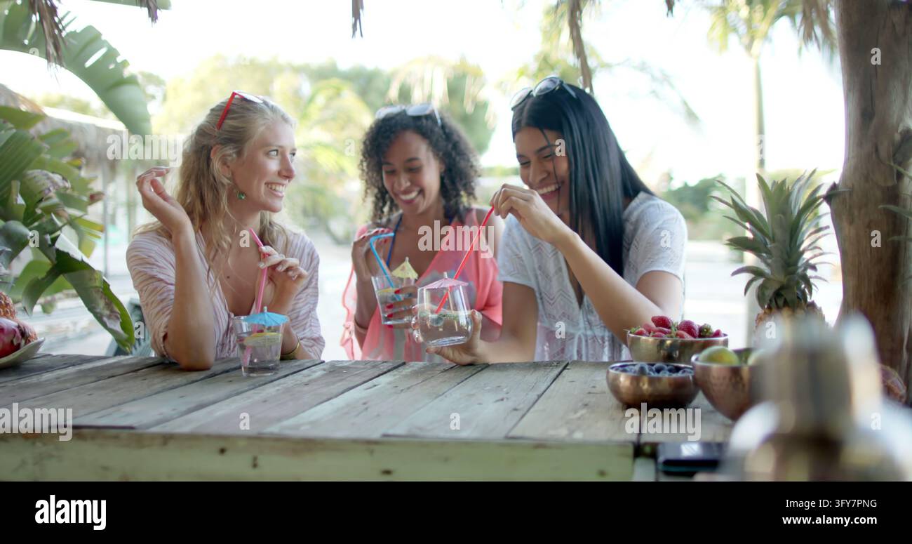 Amies diverses et heureuses buvant des cocktails dans un bar de plage et discutant. Vacances, temps libre, été et amitié. Banque D'Images