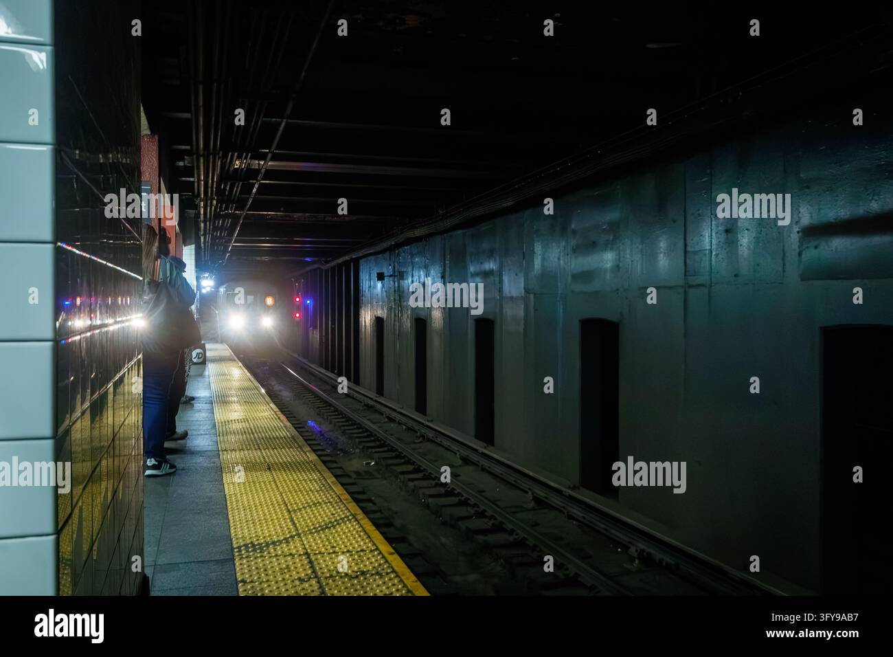 Train de métro de New York City approchant le quai à une station avec un passager en attente Banque D'Images