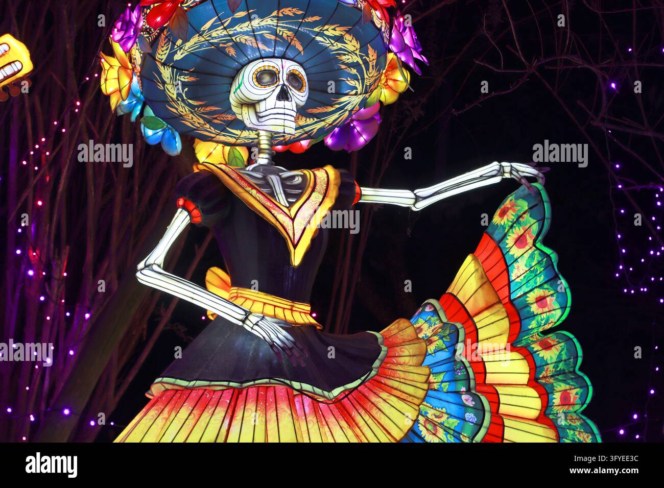 Sculpture de lanterne lumineuse d’un squelette Catrina portant un chapeau fleuri et une jupe colorée à volants, dansant la nuit. Convient pour le Jour des Morts, Halloween Banque D'Images