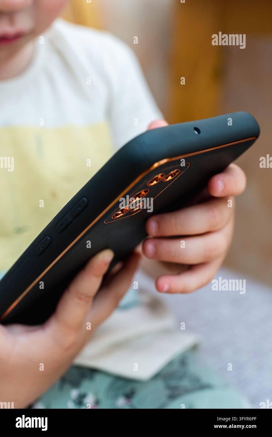 Grossissement des mains d'un enfant tenant un smartphone noir. Banque D'Images