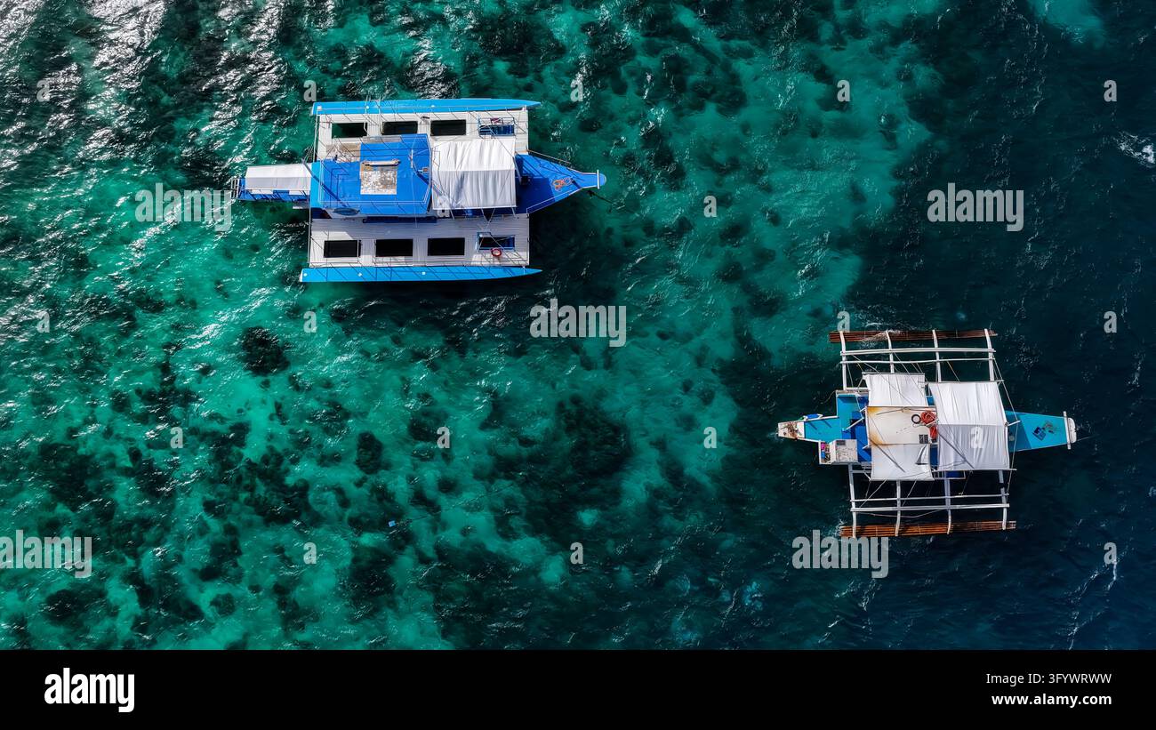 Vue aérienne de deux bateaux à balanciers traditionnels flottant sur les eaux turquoise claires d'un récif corallien à Maasin, Southern Leyte, Philippines. Banque D'Images