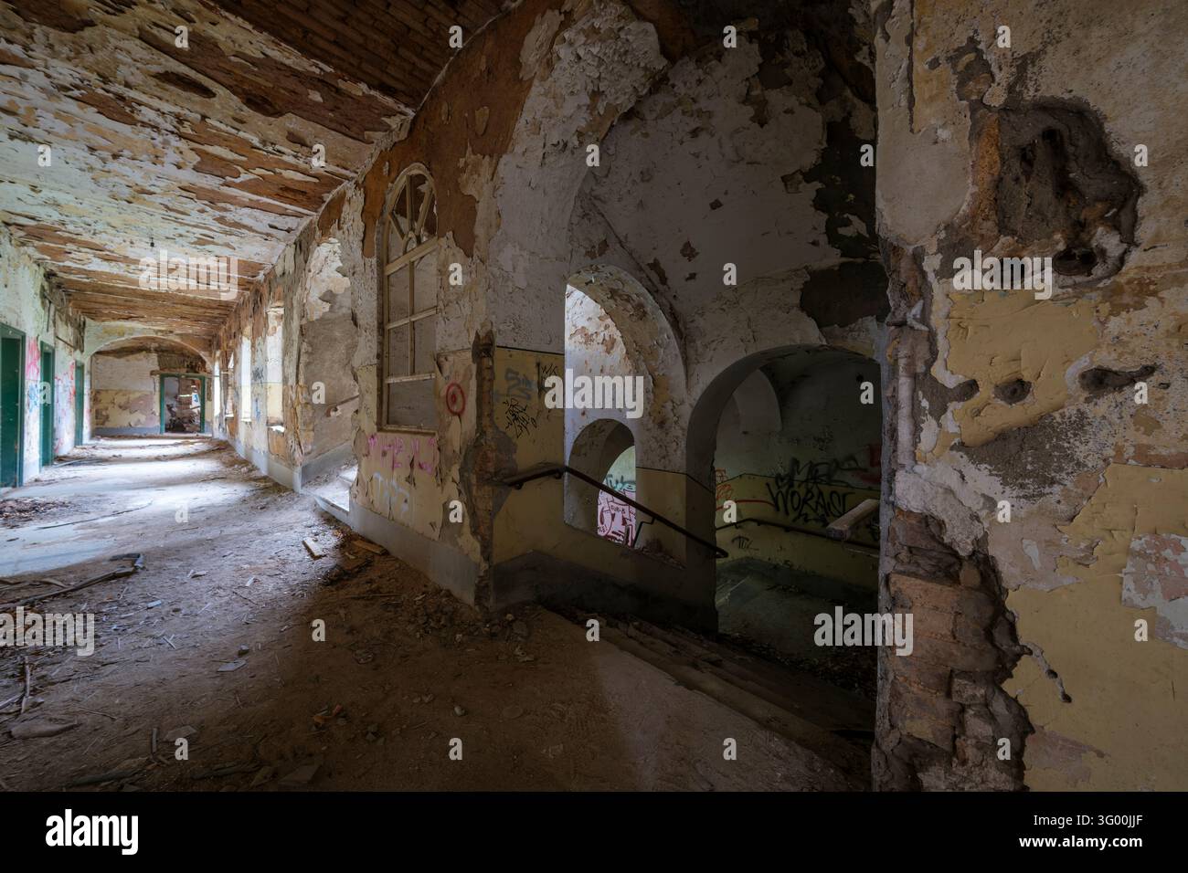 Un couloir endommagé à l'intérieur de la caserne abandonnée de Jajce à Sarajevo présente des murs en plâtre écaillés et des ouvertures en arc. Banque D'Images