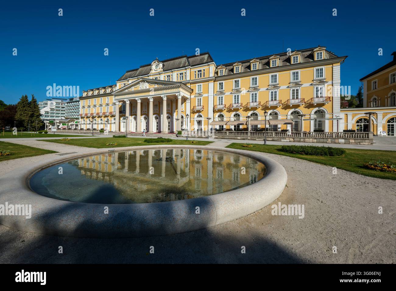Un bassin d'eau circulaire en pierre reflète la façade jaune du Grand Hotel Rogaška dans un cadre de parc à Rogaška Slatina. Banque D'Images