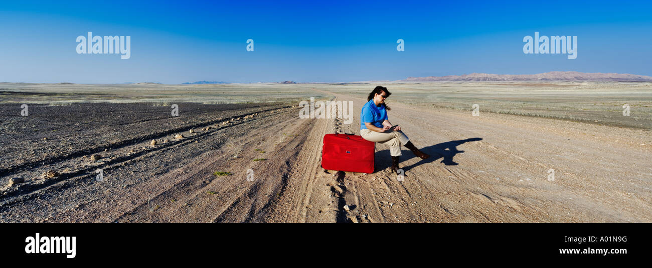 Une femme assise sur une valise rouge ses ongles remplissage entouré par de vastes paysages arides de la Namibie publié Modèle Banque D'Images