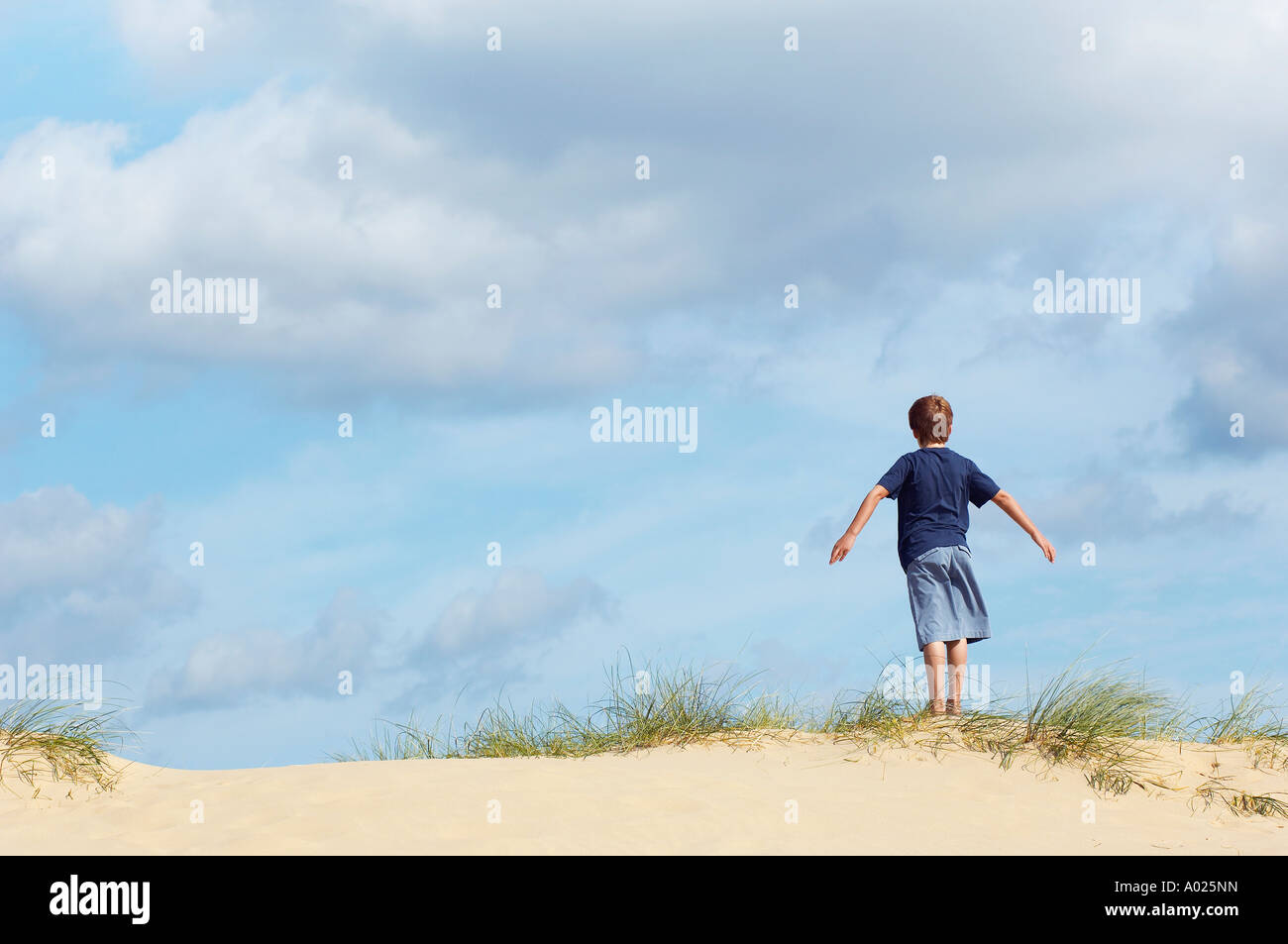 Young Boy Standing On Sand Dune Dans Le Vent Avec Les Bras Tendus Vue Arriere Photo Stock Alamy