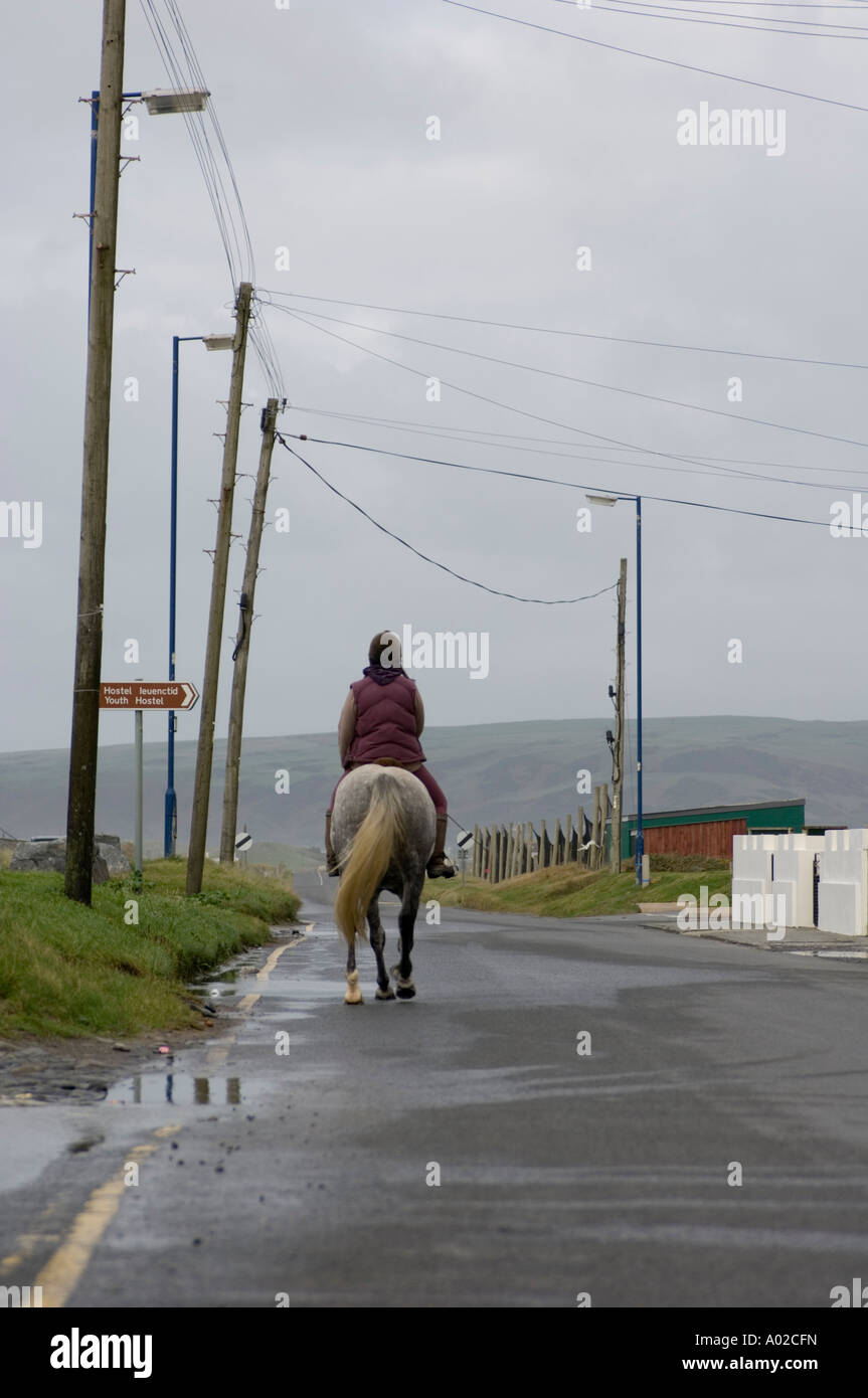 Son cheval équitation femme vide sur la route à travers le village côtier de Borth en vue de derrière, UK Banque D'Images