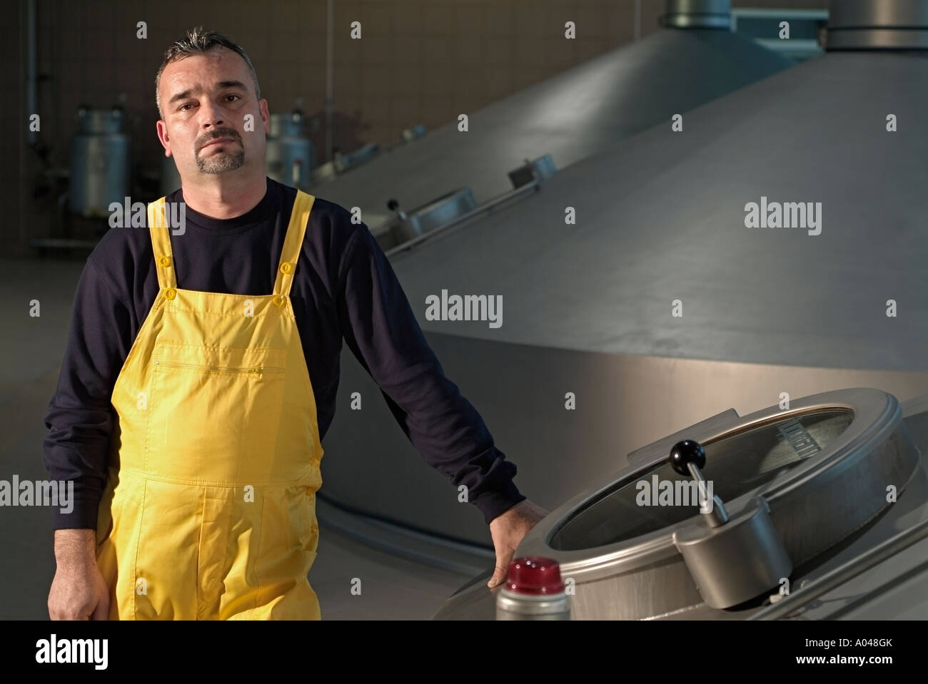 Travailleur de la brasserie debout à côté d'une grande cuve de fermentation Banque D'Images