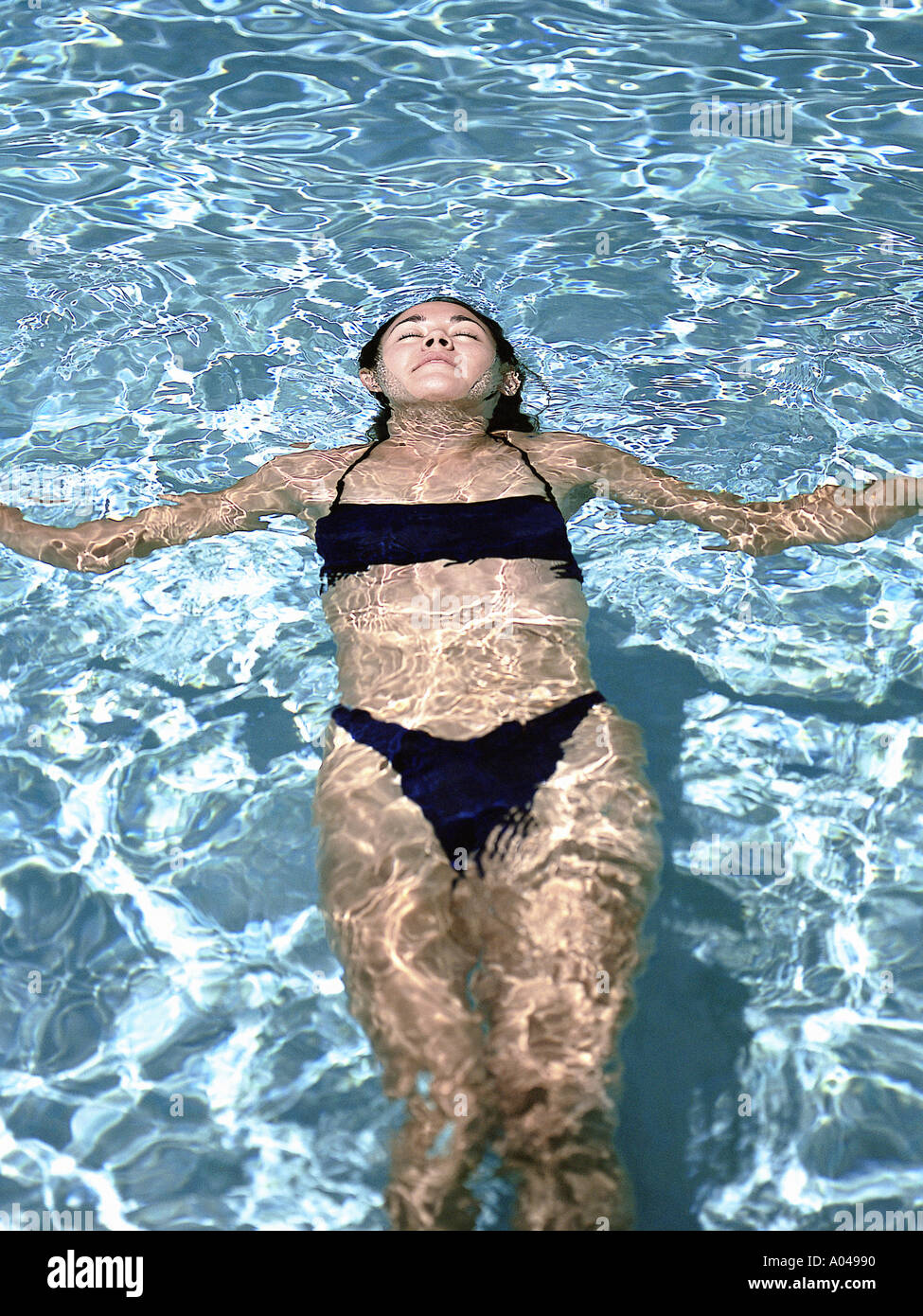 Young woman wearing bikini noir flottant sur son dos dans une piscine Banque D'Images