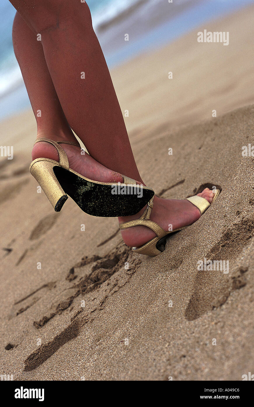 Jeune femme portant des chaussures haut talon d'or debout sur la plage Banque D'Images