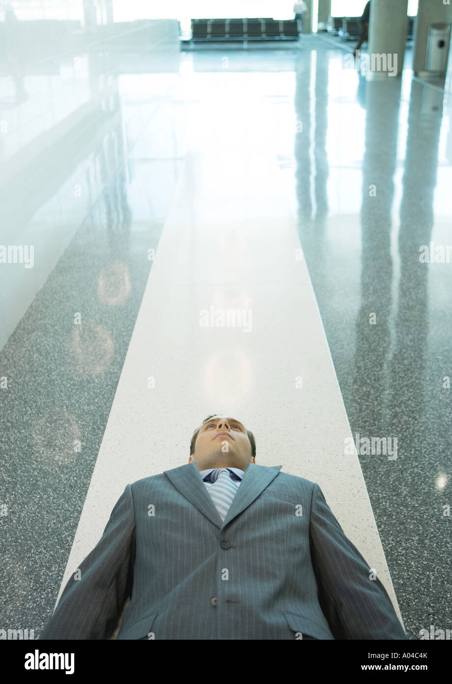 Businessman lying down on floor in airport Banque D'Images