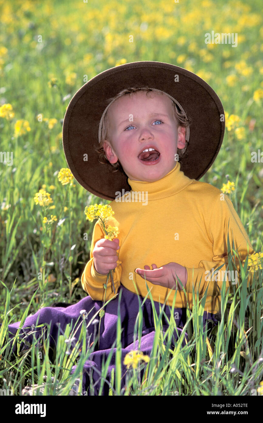 Jeune garçon de l'ouest cowboy assis dans un champ de fleurs chantant une chanson portant un chapeau de cowboy Banque D'Images